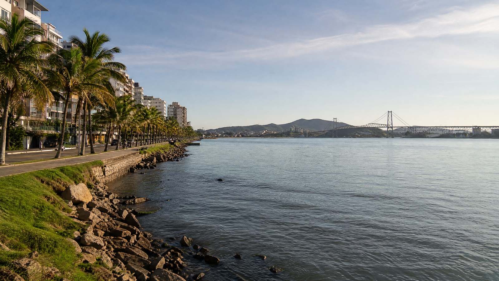 Calçadão de Coqueiros, no Continente, com palmeiras e a vista da baía para a Ilha e a ponte Hercílio Luz.