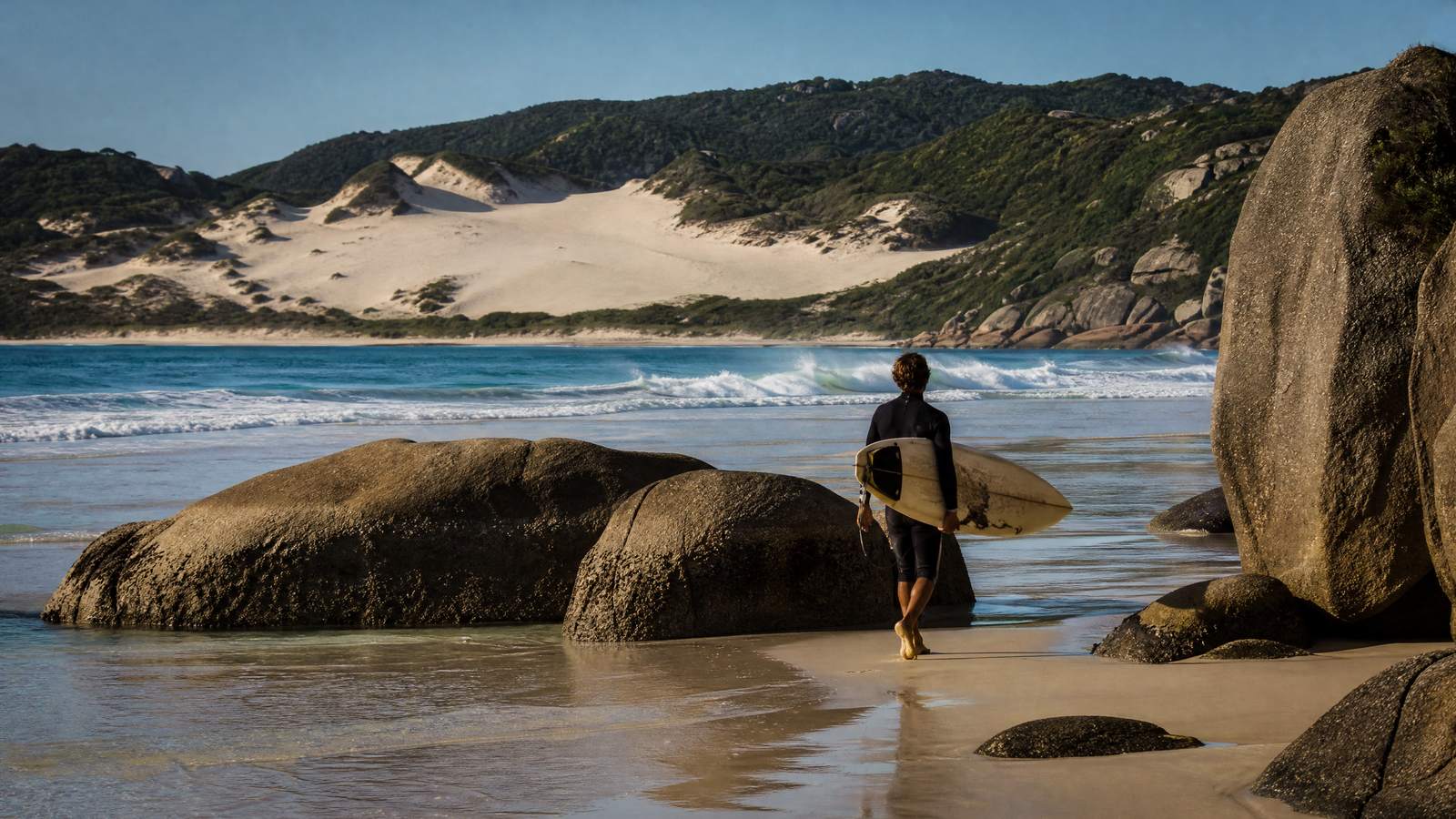 As pedras da Joaquina com um surfista de costas e as dunas atrás.
