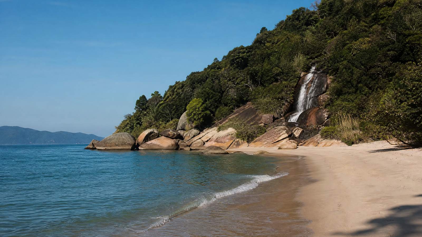 A Praia da Solidão, tranquila entre morros, com uma cachoeira perto.